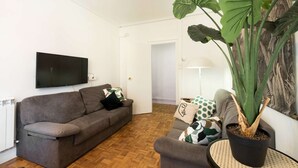 A living room with a grey sofa, a flat-screen TV, a large potted plant, and a patterned wall. - Spacious, family-friendly apartment right on Zurriola Beach (Donostia)