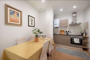 A compact kitchen with modern appliances, a dining area with a table and chairs, and a framed picture on the wall.