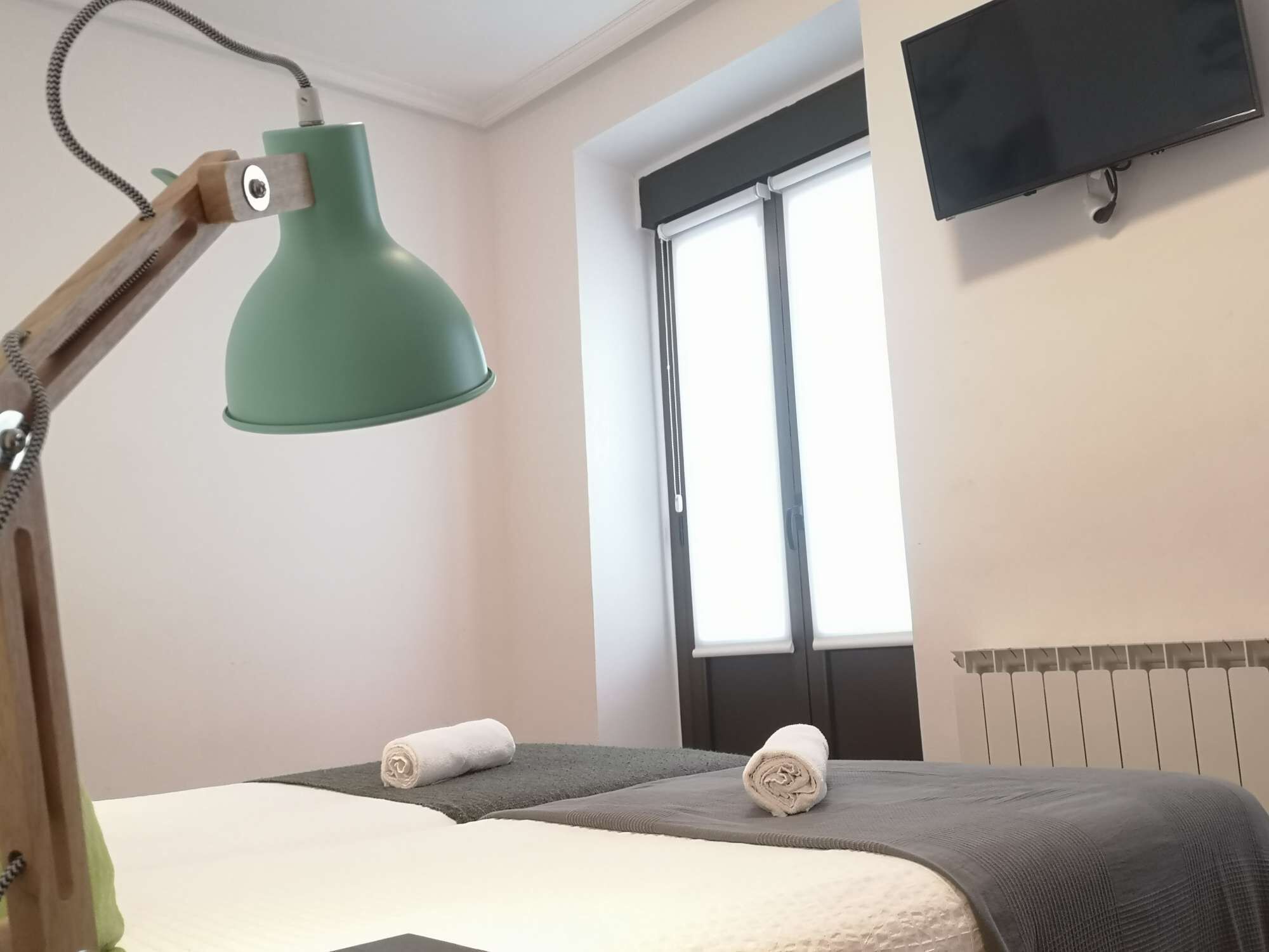 Une chambre avec un lit, une lampe de bureau verte, une fenêtre et un téléviseur fixé au mur.