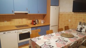 Une cuisine compacte avec des meubles bleus, un réfrigérateur blanc et une table dressée avec une nappe ornée de motifs parisiens.