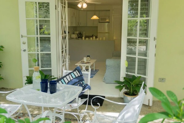 An open-plan living and dining area with a kitchen, white furniture, and potted plants.