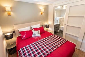 Une chambre d’hôtel avec un lit, des lampes de chevet, une couverture à carreaux et un miroir qui reflète la salle de bain.