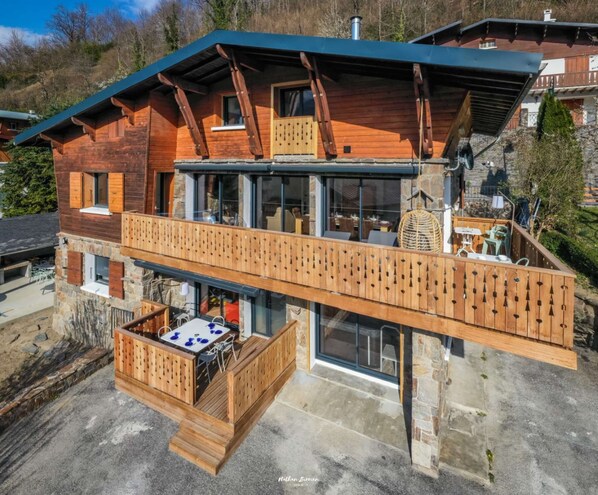 Un chalet en bois doté d’un balcon, de fondations en pierre et d’un coin repas avec des sièges extérieurs.