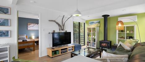 Een moderne woonkamer met een flatscreen televisie, een glazen salontafel, een bank, een houten kast en een boekenkast.