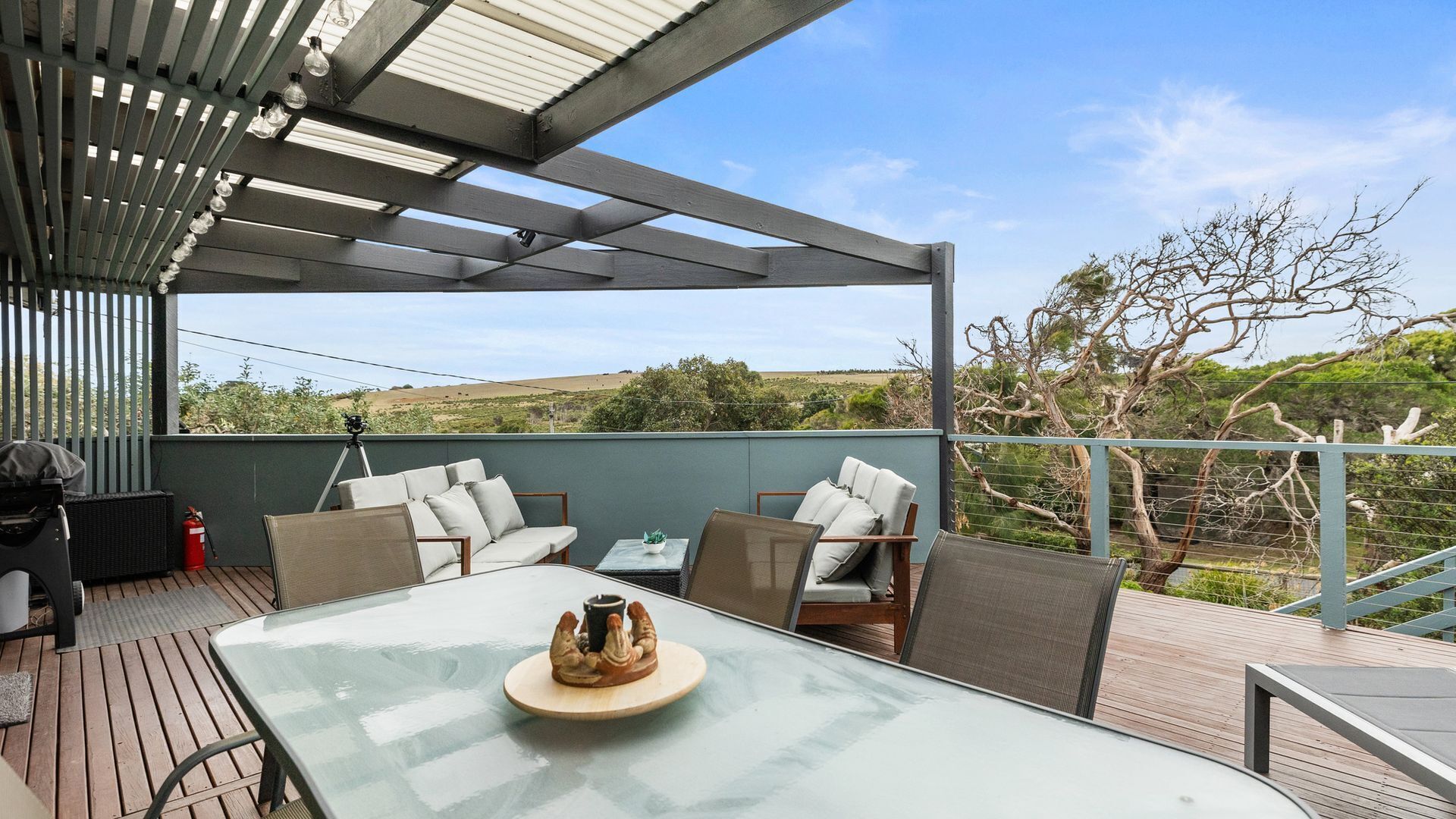 An outdoor patio with a glass table, wicker chairs, and a view of the countryside.