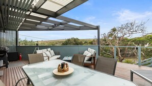 Un patio al aire libre con mesa de vidrio, sillas de mimbre y vista al campo.