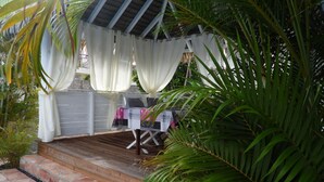 Un patio al aire libre con terraza de madera, cortinas blancas y una mesa lista para comer.