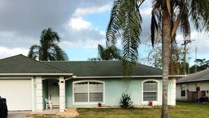 Uma casa térrea com garagem, um pequeno jardim frontal e uma palmeira.