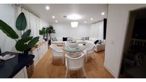 A modern living room with a glass-top dining table, white sofas, and a large potted plant. - Luxurious Oceanfront Ormond Getaway (Ormond Beach)