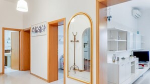 Ein modernes Hotelzimmer mit einer Holztür, einem großen Spiegel mit goldener Rahmung, einem weißen Schrank und einem Fernseher.