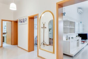 A modern hotel room with a wooden door, a large mirror with a gold frame, a white cabinet, and a television.