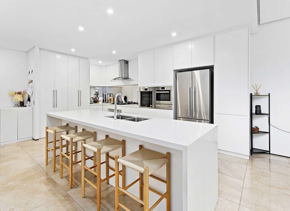 A modern kitchen with white cabinetry, stainless steel appliances, and a central island with bar stools.