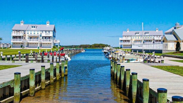 Una propiedad frente al mar con un muelle de madera largo que conduce a un puerto deportivo, rodeada por dos edificios grandes con balcones.