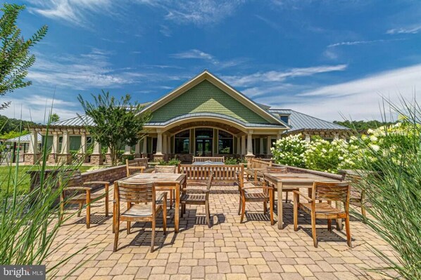 A building with a green roof and a covered patio area with wooden furniture. - Beach Home in the Beautiful Forest Landing at Bethany Beach Community (Frankford)