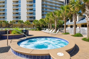 A hot tub surrounded by lounge chairs and palm trees, with a building in the background. - Mainsail 351 - Gulf Front, Free Beach Service, Heated Pool, Tennis + Fitness! (Miramar Beach)