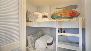 Ein Stockbett, ein Deckenventilator, ein Surfbrett und Handtücher mit der Aufschrift 'Ocean Breeze'.
