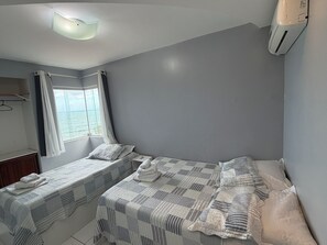 Une chambre avec deux lits, une fenêtre avec des rideaux, un luminaire suspendu et un appareil de climatisation.