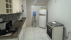 Una cocina compacta con armarios blancos, microondas integrado, dispensador de agua y horno pequeño.