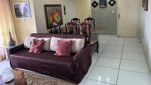 Una sala de estar con un sofá marrón, una mesa de comedor con sillas, una lámpara de araña y cuadros en las paredes.