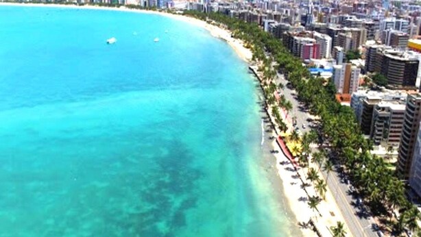 Vista aérea de una ciudad costera con playa, rascacielos y un mar azul cristalino.
