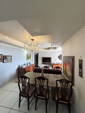 A dining area with a central island, chairs, a chandelier, and a television in the background. - Saint Thomaz a Beira mar da Jatiuca (AL)