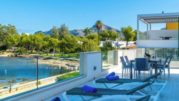 A rooftop terrace with sun loungers, a dining area, and a view of the sea and mountains.