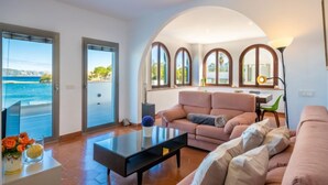 A modern living room with a sofa, a coffee table, and a view of the sea through large windows.