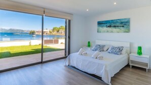 A bedroom with a large sliding glass door leading to a balcony with a view of the sea and buildings.