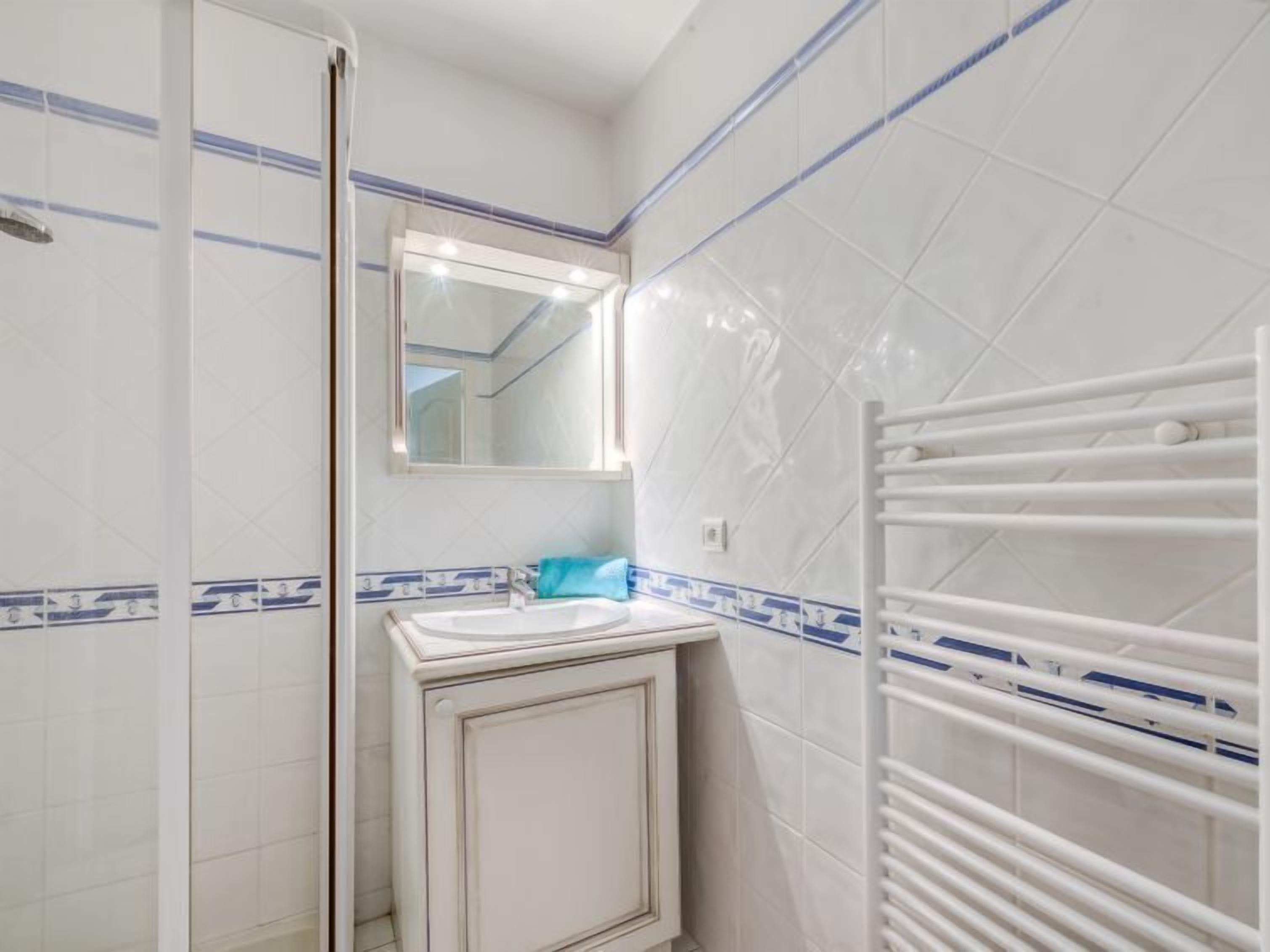 A bathroom with white tiles, a sink, a mirror, and a towel rack.