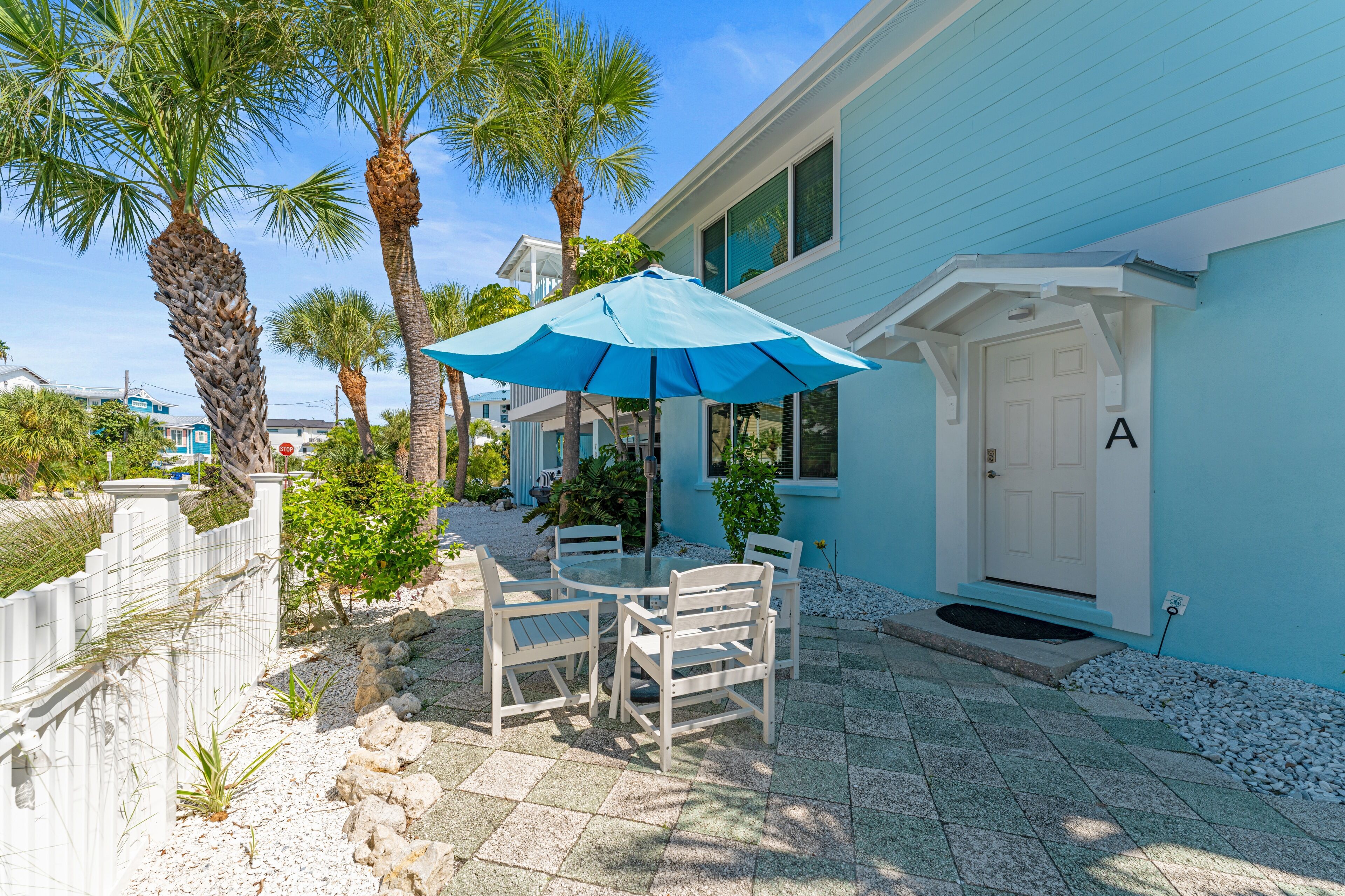 A patio with a table and chairs, a blue umbrella, and a white door with the letter 'A' on it.