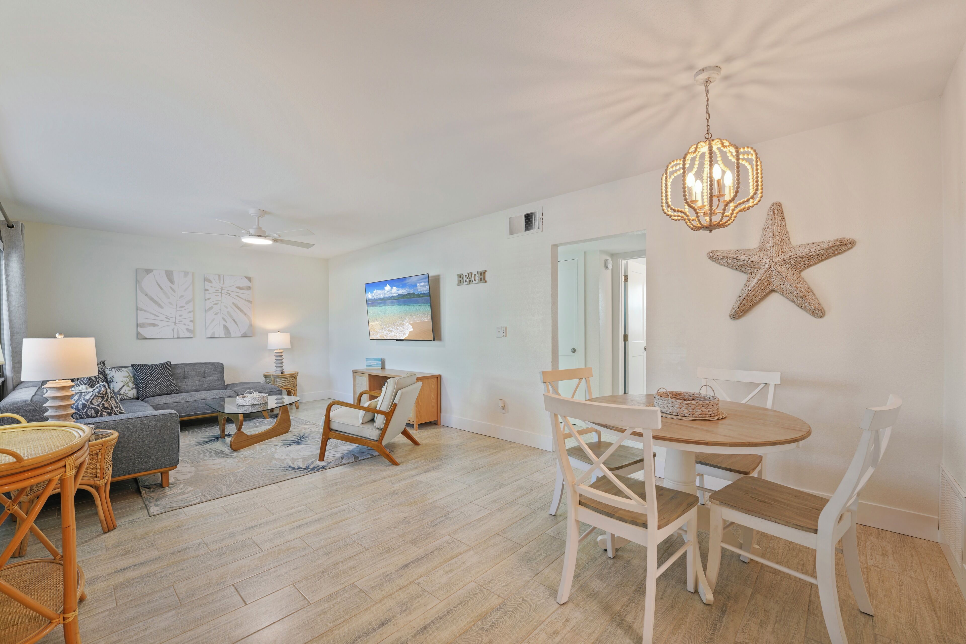 A spacious living area with a sofa, coffee table, and dining table. There is a ceiling fan, wall art, and a starfish decoration.