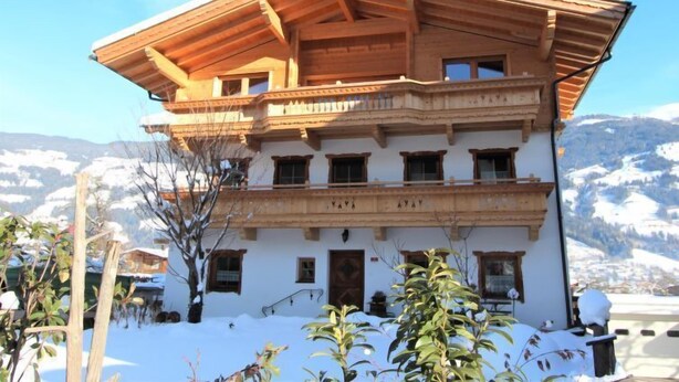 A multi-story building with a wooden roof and balconies, surrounded by snow-covered mountains.