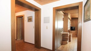 A hallway with wooden flooring and walls, leading to a kitchen area with wooden cabinets and a television.