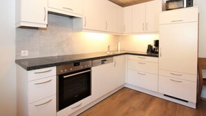 A modern kitchen with white cabinets, a built-in oven, a microwave, and a coffee maker.