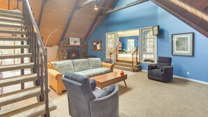 A spacious loft with a high ceiling, a wooden staircase, a cozy seating area with a sofa and armchairs, a fireplace, and a large mirror reflecting the room. - Riverfront Retreat in Nathrop: Fire Pits & Hot Tub (Nathrop)