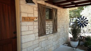 A stone building with a wooden door, a sign reading "Tres Leches," and a windmill. - Bakery Haus- Tres Leches | Pleasant Cabin for 2 (Fredericksburg)