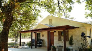 A stone house with a covered patio, outdoor seating, and a windmill. - Bakery Haus- Tres Leches | Pleasant Cabin for 2 (Fredericksburg)