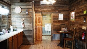 A rustic wooden interior with a kitchen area featuring a sink, cabinets, and a dining table with chairs. - Bakery Haus- Tres Leches | Pleasant Cabin for 2 (Fredericksburg)