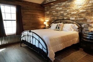 Ein Schlafzimmer mit einer Steinsandsteinwand, einem Bett mit Metallgestell, einem Fenster mit Vorhängen und einem Nachttisch mit Lampe.