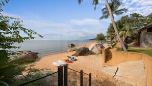 Une plage avec un escalier menant à un bâtiment, des palmiers et des kayaks sur le sable.