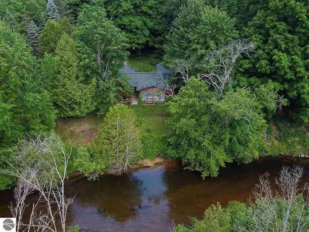 A house surrounded by dense forest and a small stream.