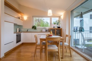 A modern kitchen with wooden cabinets, a dining table with chairs, and a large window providing a view of the outdoors.