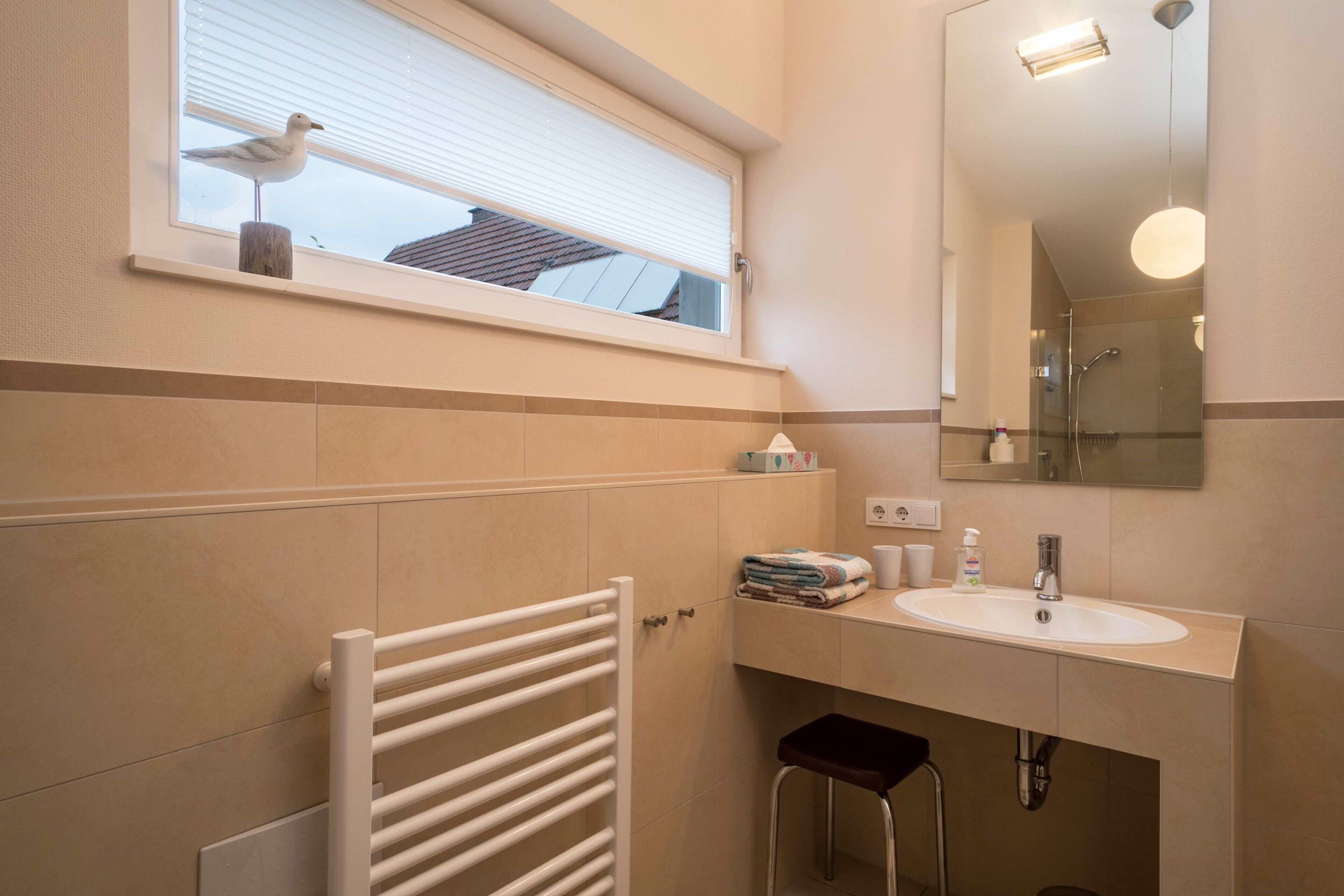 A bathroom with a window, a towel rack, a sink, and a mirror.