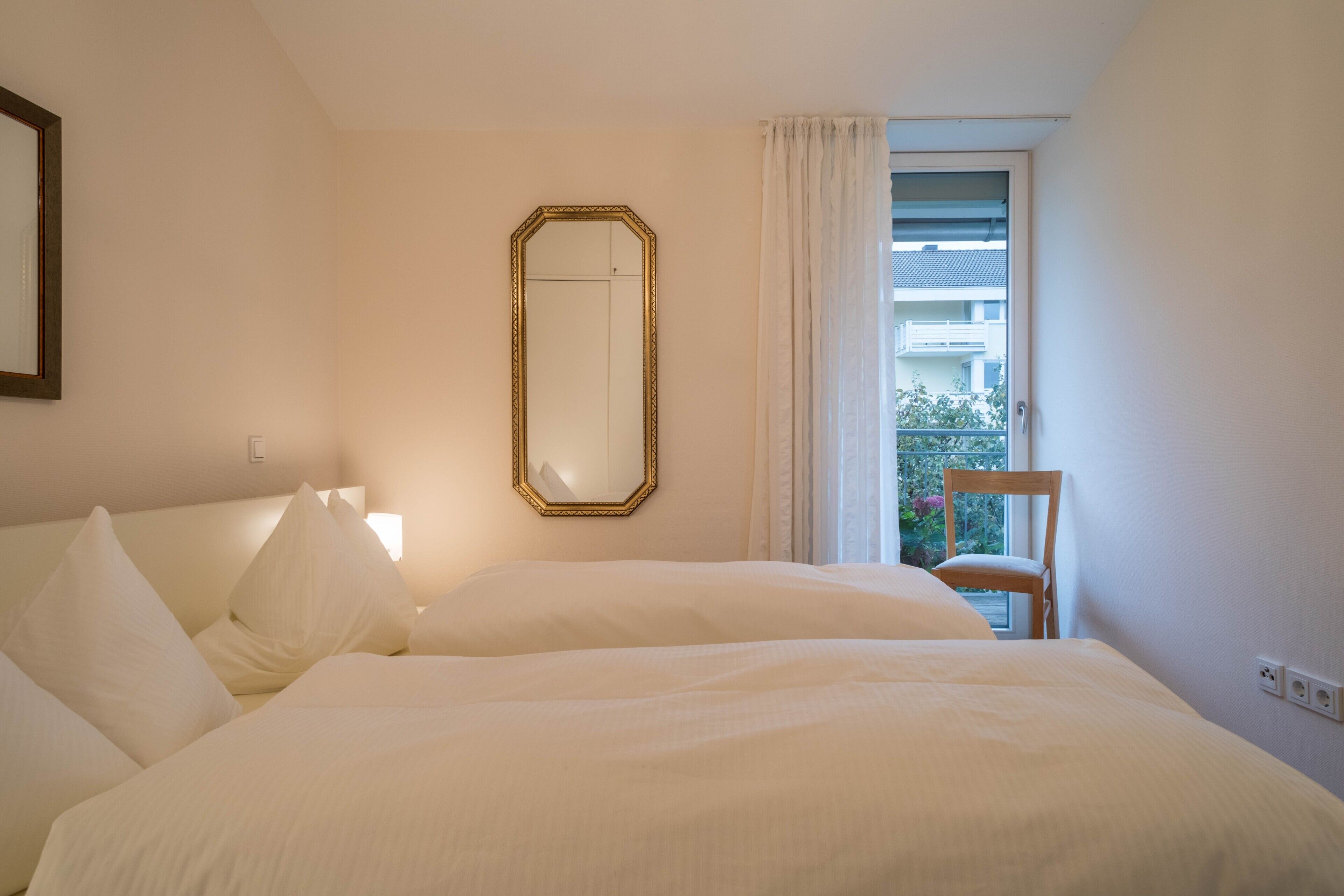 Habitación de hotel con cama, espejo, silla y ventana con vista a edificios.