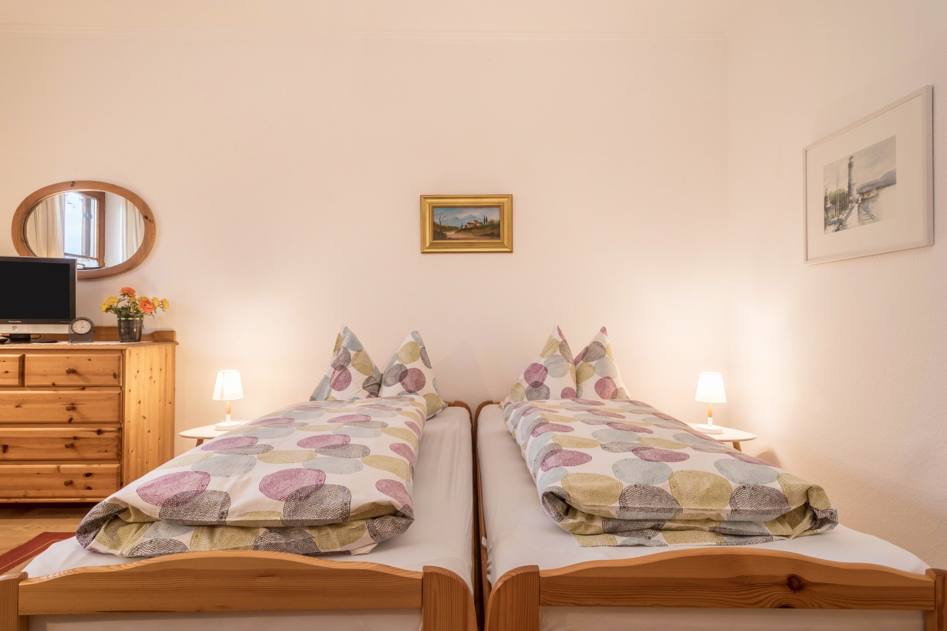 A bedroom with two beds, a dresser, a mirror, and two wall-mounted lamps.