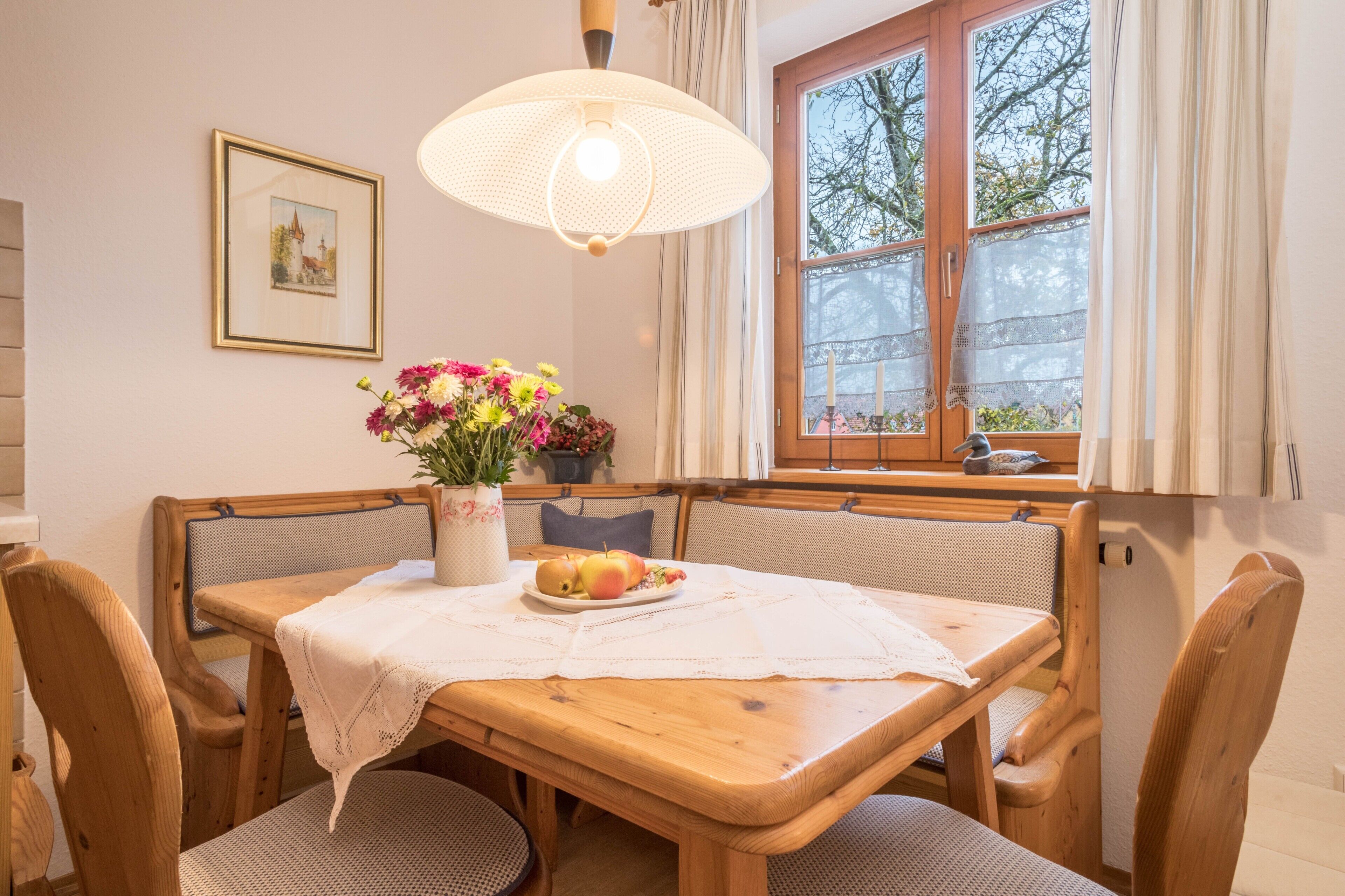 Ein Essbereich mit Holztisch, Stühlen, einer Vase mit Blumen und einem Fenster mit Vorhängen.