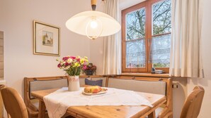 Un comedor con una mesa de madera, sillas, un florero con flores y una ventana con cortinas.