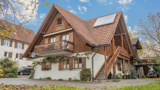 Una casa de madera de dos pisos, con balcón, escaleras y garaje.