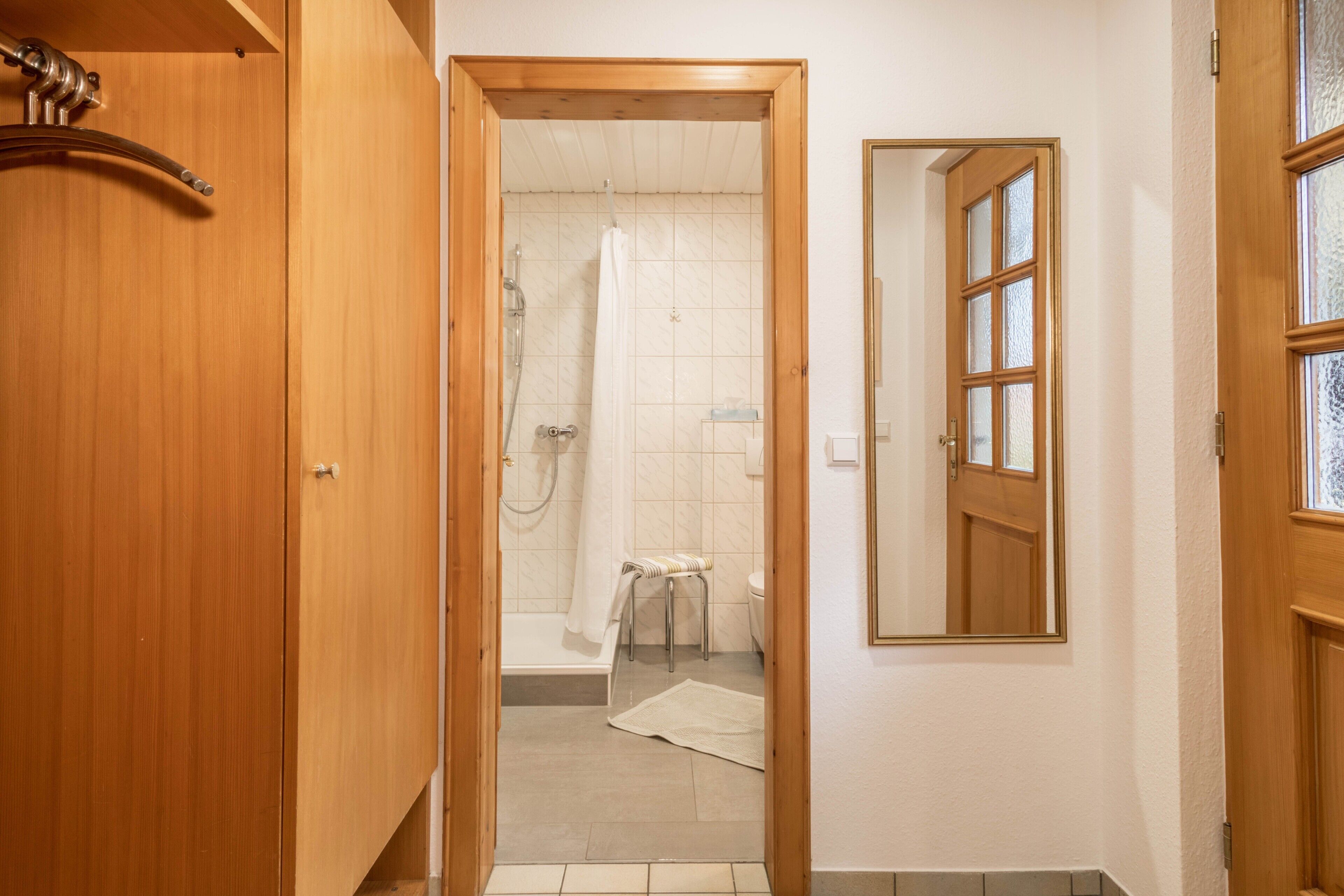 Eine Holztür zu einem Badezimmer mit Dusche, Toilette und einem Spiegel an der Wand.