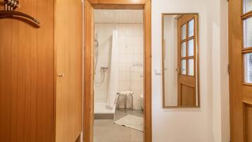 Eine Holztür zu einem Badezimmer mit Dusche, Toilette und einem Spiegel an der Wand.